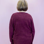 Person wearing a maroon sweater and pants against a light purple background