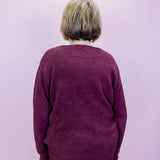 Person wearing a maroon sweater and pants against a light purple background