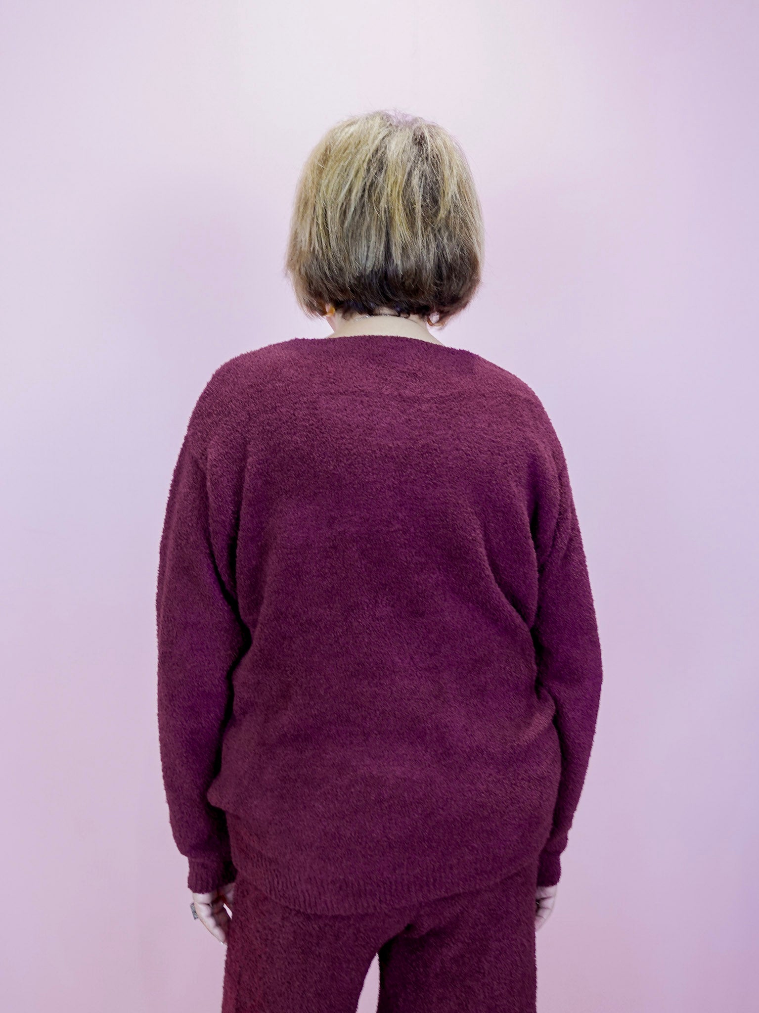 Person wearing a maroon sweater and pants against a light purple background