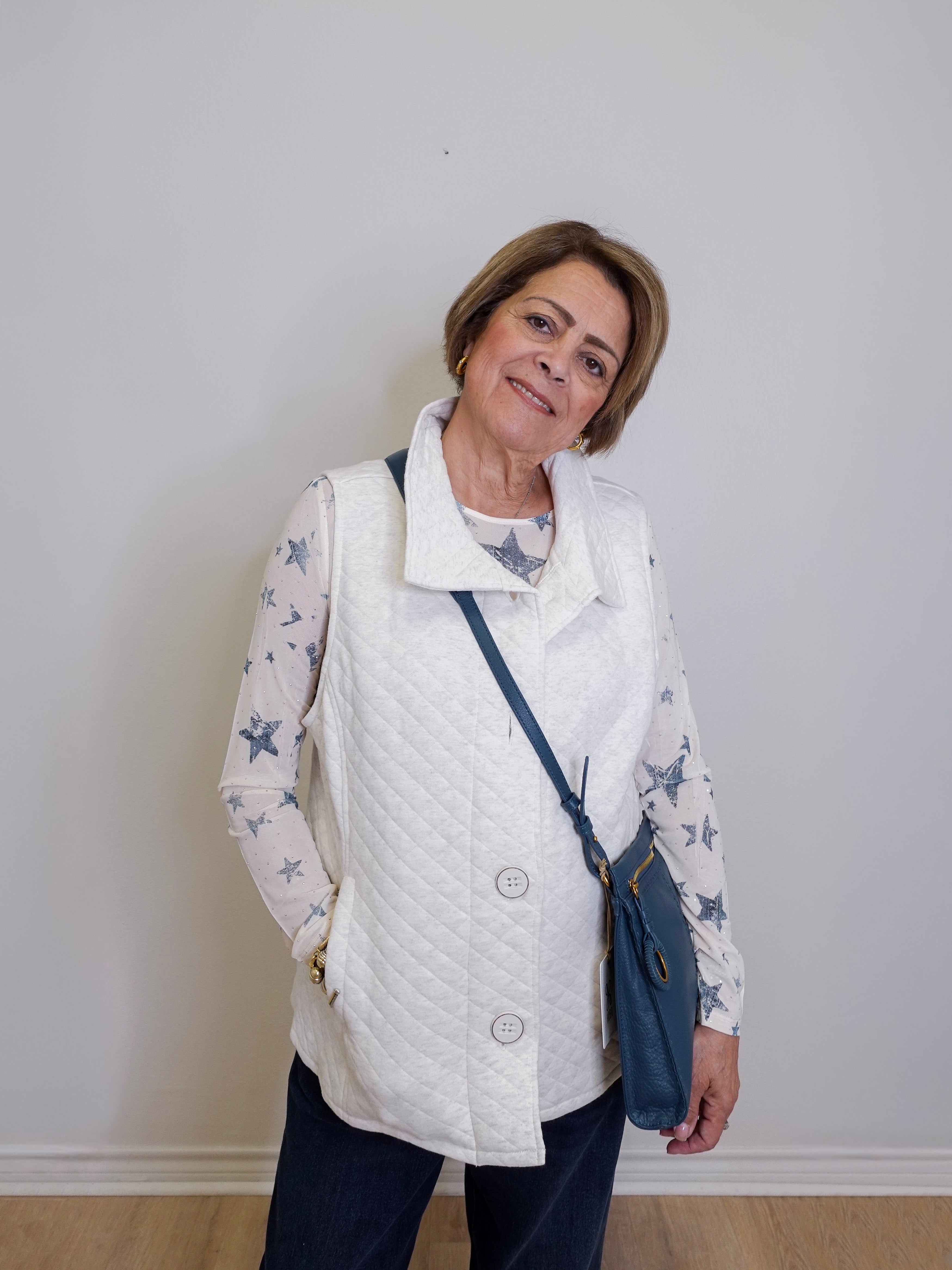 Woman wearing a white quilted vest over a star-patterned shirt with a blue crossbody bag against a plain background.