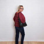Woman wearing a red sweater and black pants standing against a white wall.