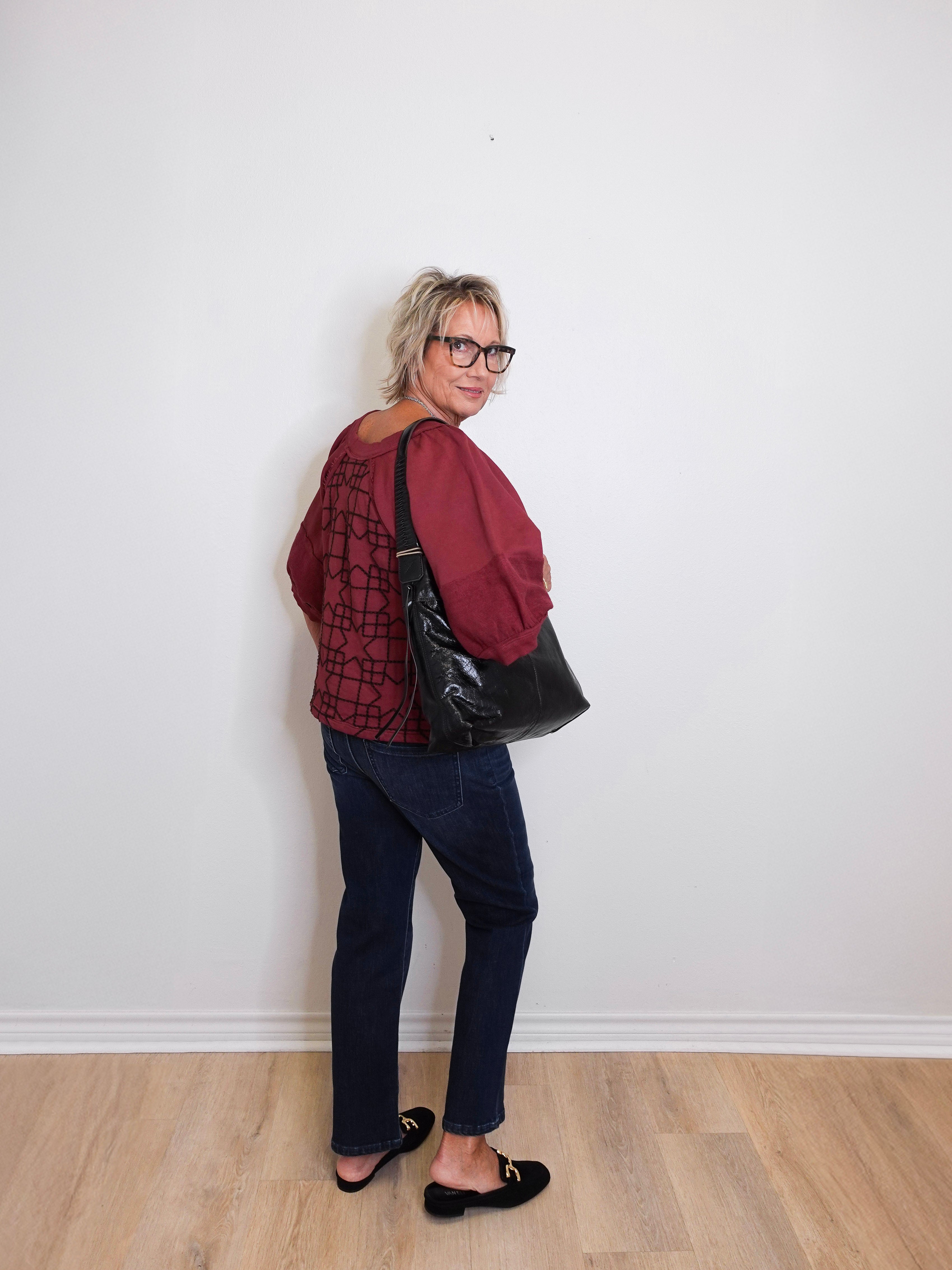 Woman wearing a red sweater and black pants standing against a white wall.