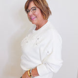 woman wearing a white cream embroidered flower sweater against. a white background. 