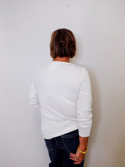 Person wearing a white long sleeve top and dark jeans against a plain wall