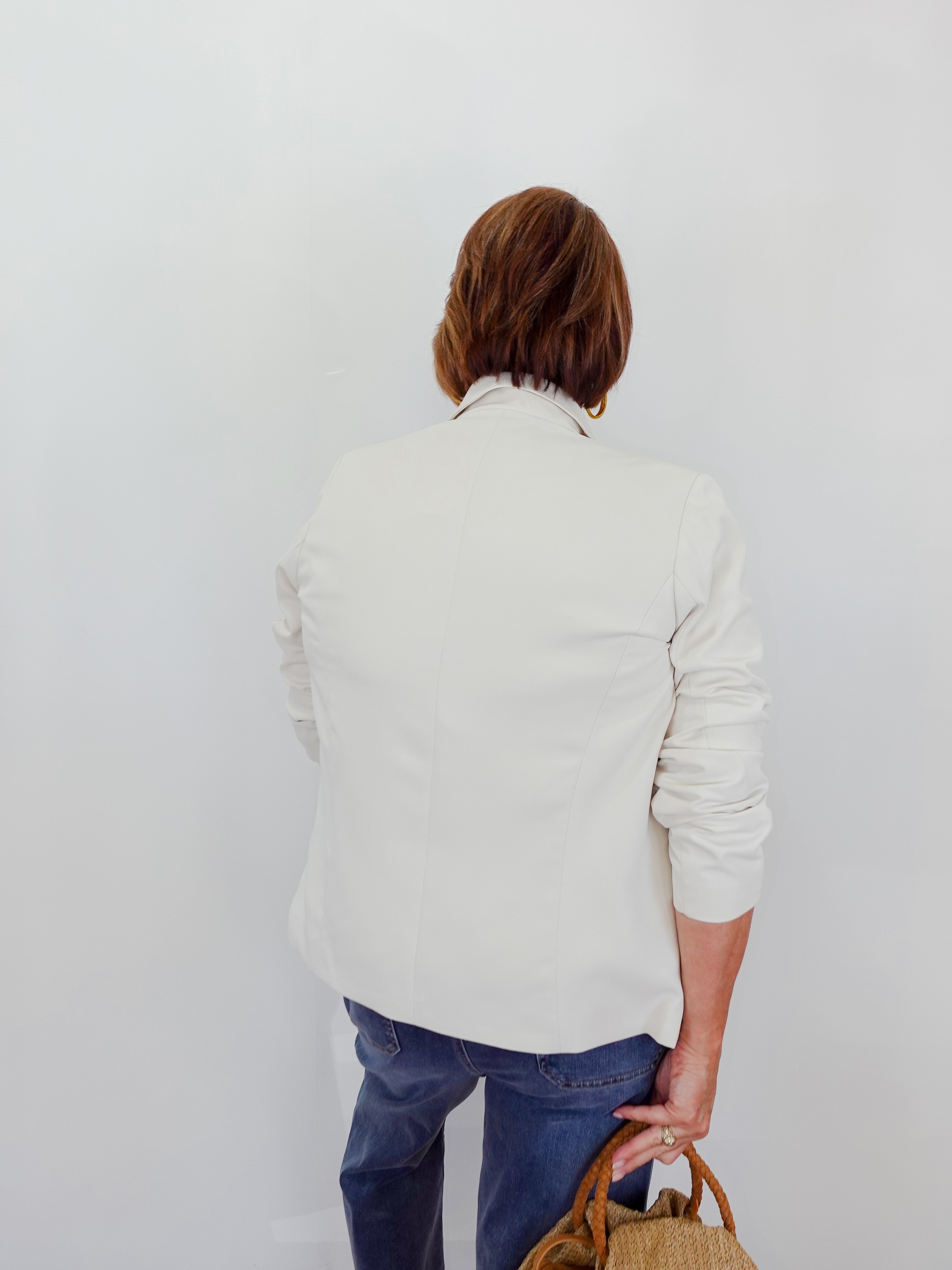 Person wearing a light-colored sweater and blue jeans, holding a brown bag against a white background