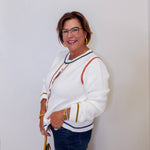 Woman wearing a white sweater with colorful accents against a plain background