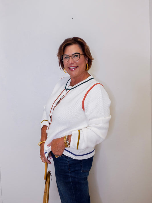 Woman wearing a white sweater with colorful accents against a plain background