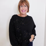 Woman wearing a black sweater with floral embellishments against a white background