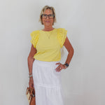 Woman wearing a yellow top and white skirt against a plain background