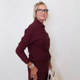 Woman wearing a burgundy outfit with a white wall background