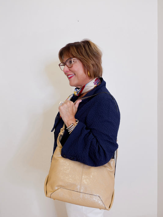 Woman holding a beige handbag against a plain background