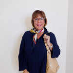 Woman wearing a navy cardigan, white pants, and holding a beige handbag against a plain background