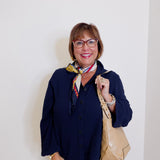 Woman wearing a navy cardigan, white pants, and holding a beige handbag against a plain background