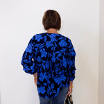 Person wearing a blue floral blouse against a white wall