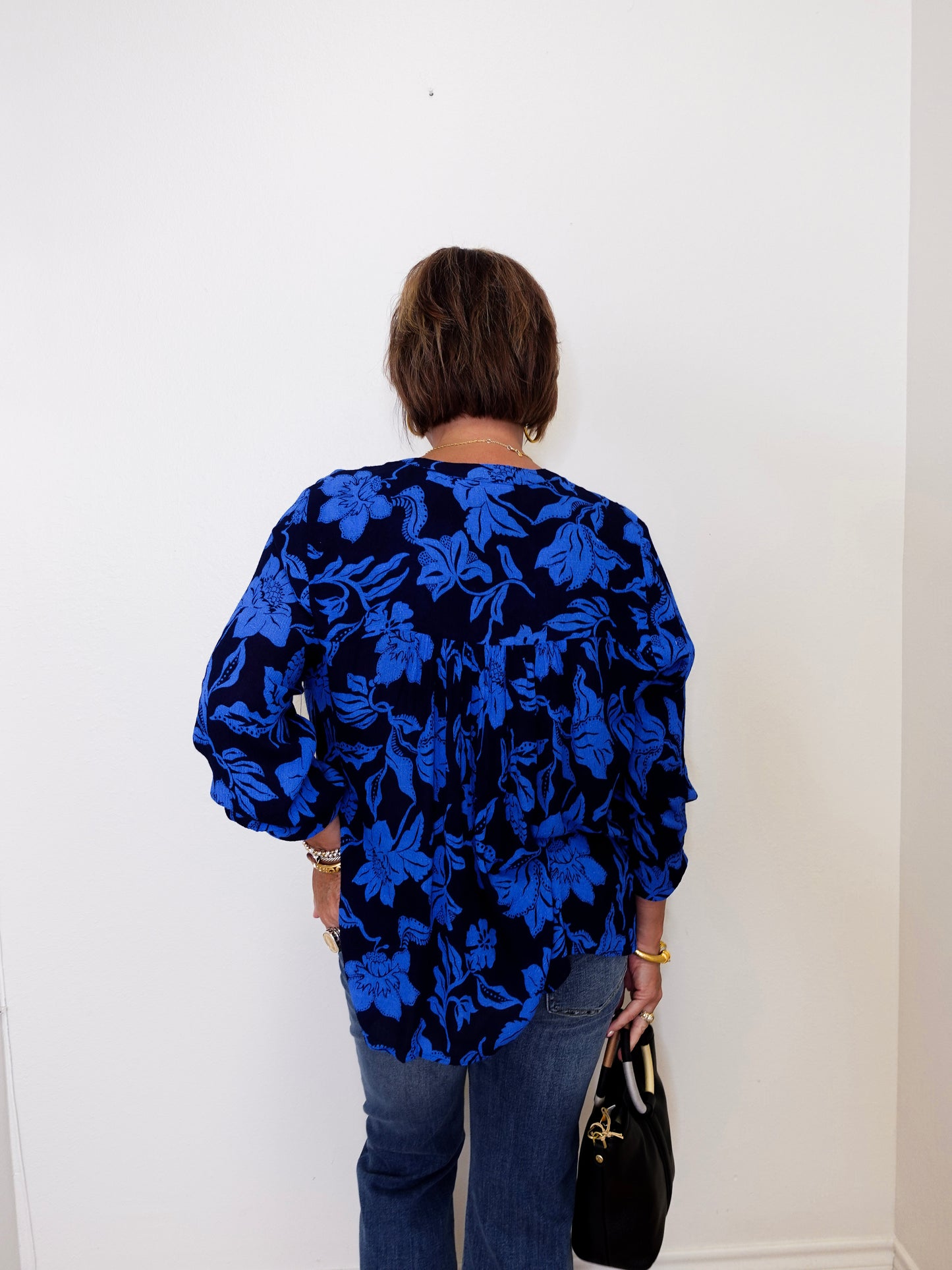 Person wearing a blue floral blouse against a white wall