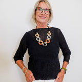 Woman wearing a black top and white pants with a colorful necklace against a plain background