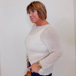 Woman wearing a light gray sweater and dark blue jeans against a white background