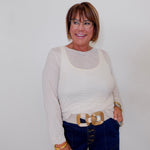Woman wearing a white top and blue jeans with a gold belt, standing against a plain background.