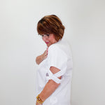 Woman wearing a white blouse with cut-out sleeves against a plain background