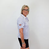 Woman wearing a light blue shirt, black shorts, and white sneakers standing against a white wall.