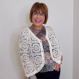 Woman wearing a white lace cardigan over a patterned top against a plain background