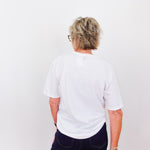 Person wearing a white t-shirt and dark pants against a plain background