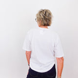 Person wearing a white t-shirt and dark pants against a plain background