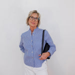 Woman wearing a blue checkered shirt and white pants against a plain background