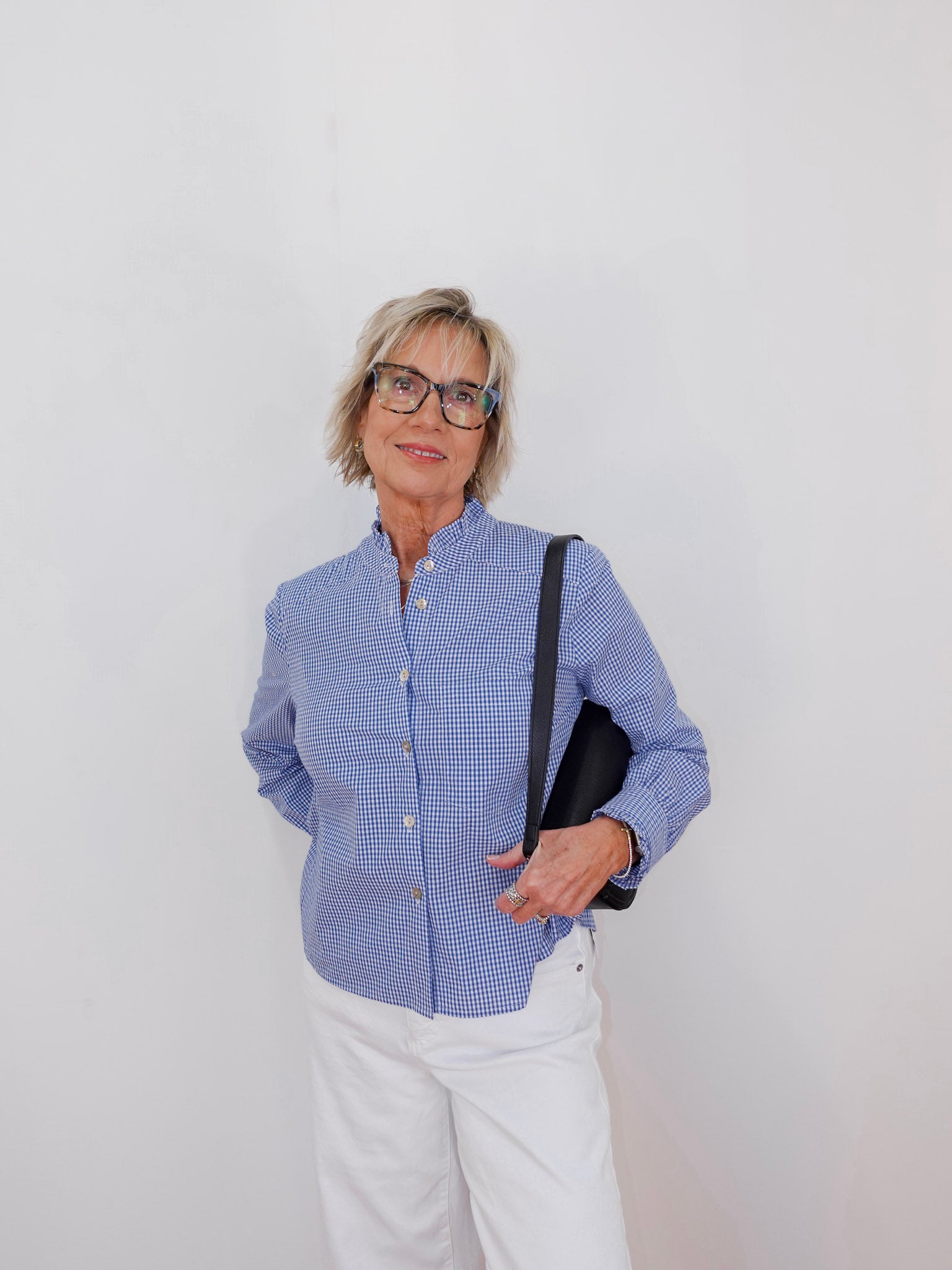 Woman wearing a blue checkered shirt and white pants against a plain background