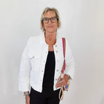 Woman wearing a white jacket and black pants, holding a red and beige bag against a plain background