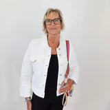 Woman wearing a white jacket and black pants, holding a red and beige bag against a plain background