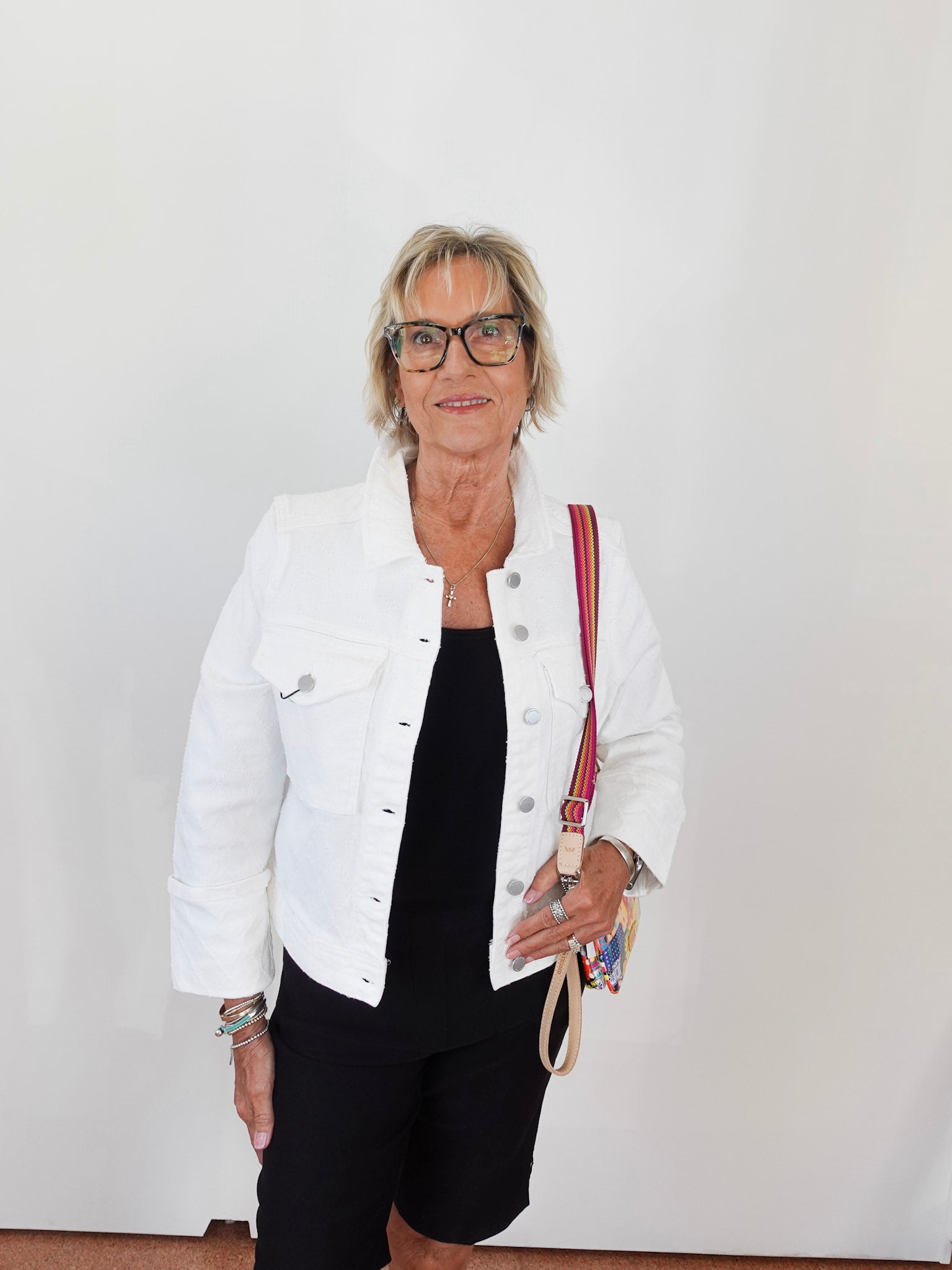 Woman wearing a white jacket and black pants, holding a red and beige bag against a plain background