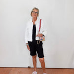 Woman wearing a white jacket, black dress, and shorts with white sneakers against a plain background.