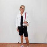 Woman wearing a white jacket, black dress, and shorts with white sneakers against a plain background.