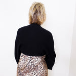 Person wearing a black sweater and leopard print skirt against a white background