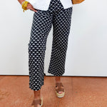 Person wearing black and white patterned pants with a white shirt and brown sandals on a beige floor.