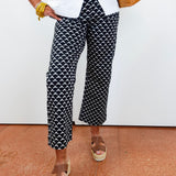 Person wearing black and white patterned pants with a white shirt and brown sandals on a beige floor.
