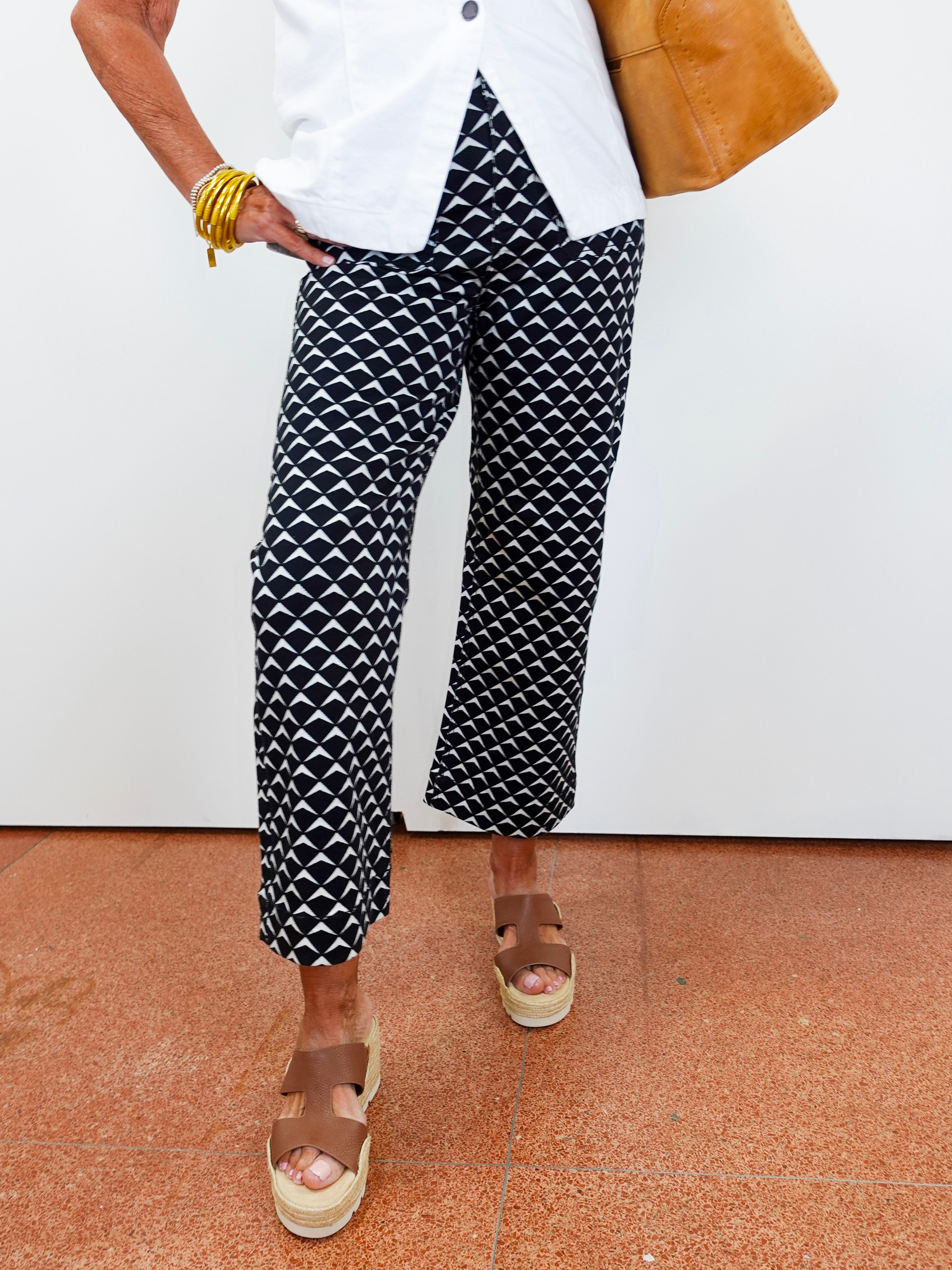 Person wearing black and white patterned pants with a white shirt and brown sandals on a beige floor.