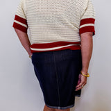 Person wearing a cream sweater with red stripes and a dark denim skirt against a white background