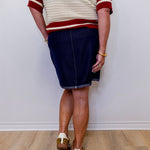 Person wearing a white and red sweater with a navy skirt on a plain background