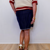 Person wearing a white and red sweater with a navy skirt on a plain background