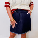 Person wearing a white sweater with red trim and a navy denim skirt against a plain background