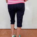 Person wearing a pink and white striped shirt, navy capri pants, and green and white shoes on a white background.