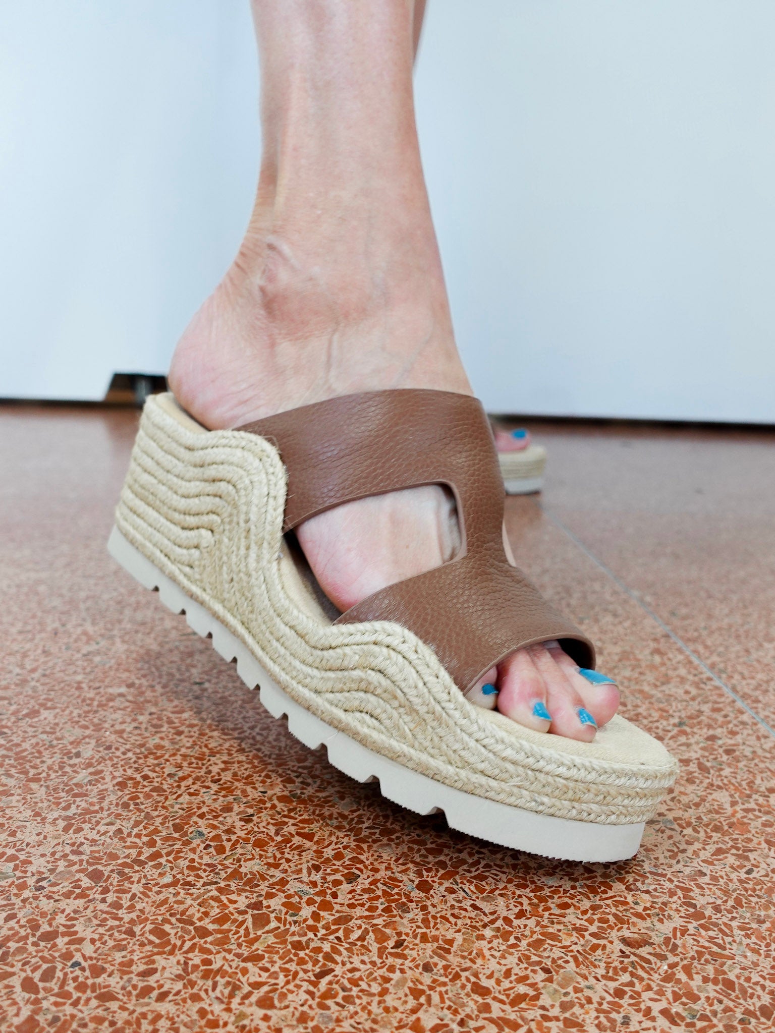 Brown wedge sandal on a foot with a white background