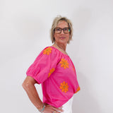 Woman wearing a bright pink top with orange floral patterns on a white background