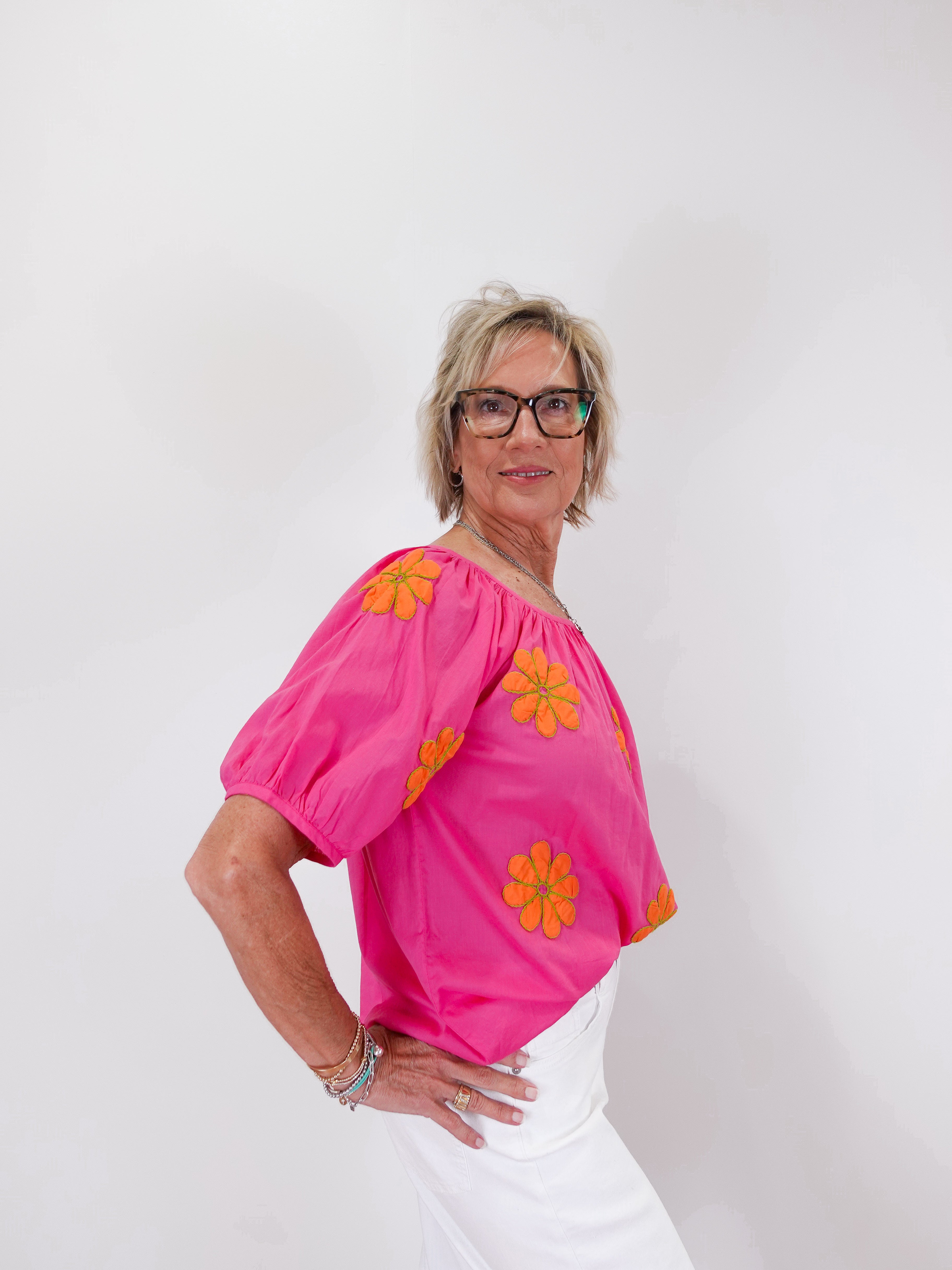 Woman wearing a bright pink top with orange floral patterns on a white background