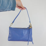 Blue handbag held by a person against a plain background