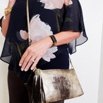 Woman holding a gold clutch purse with a floral top and black pants.