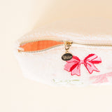 Close-up of a pouch with a pink bow and gold zipper on a light background
