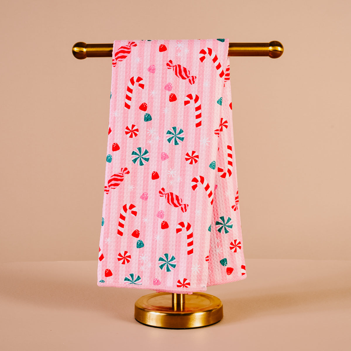 Pink towel with candy cane and snowflake pattern on a gold towel rack against a beige background